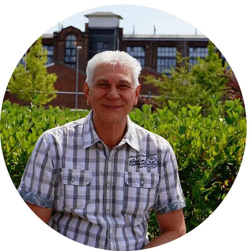 Atila-Keckes Atila Keckes, der Geschäftsführer von Pat.nrw lächelt nett in die Kamera uns sitzt vor einem grünen Busch